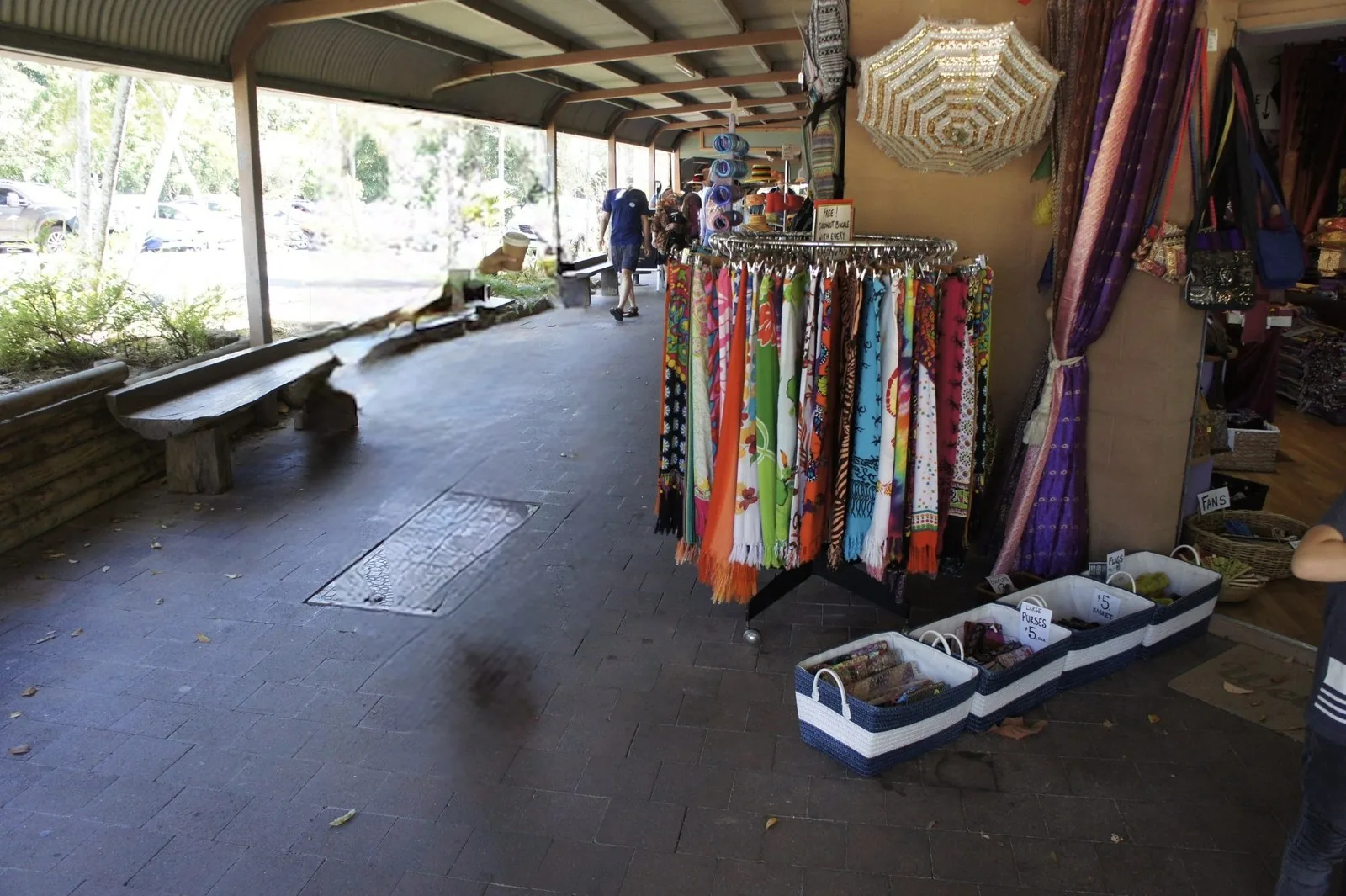 Racks of colorful fabric and price-tagged baskets in front of a shop along a covered walkway