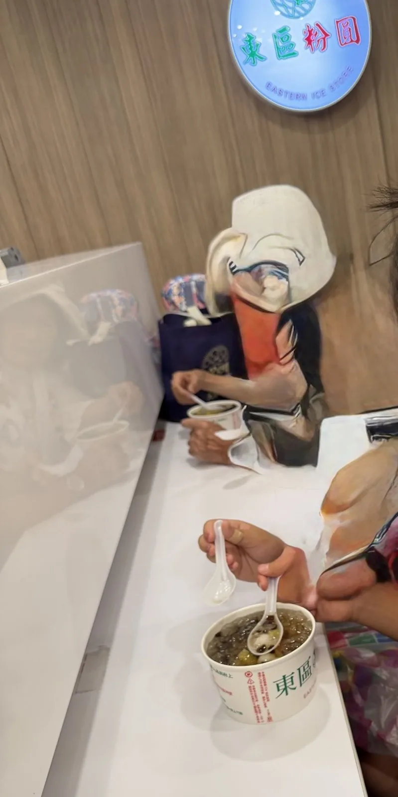 The counter inside Dongqu Fenyuan. A hand scooping a dessert of tapioca balls and taro balls from a paper cup with a spoon