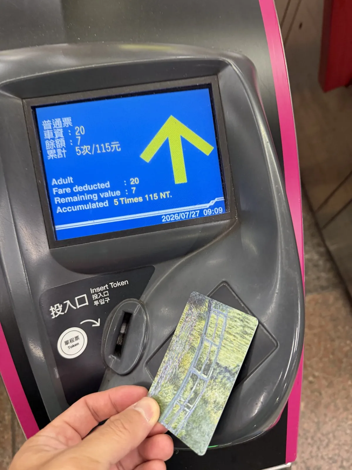 An IC card with a water lily design held to an MRT fare gate, with the screen showing a fare of NT$20 and the balance